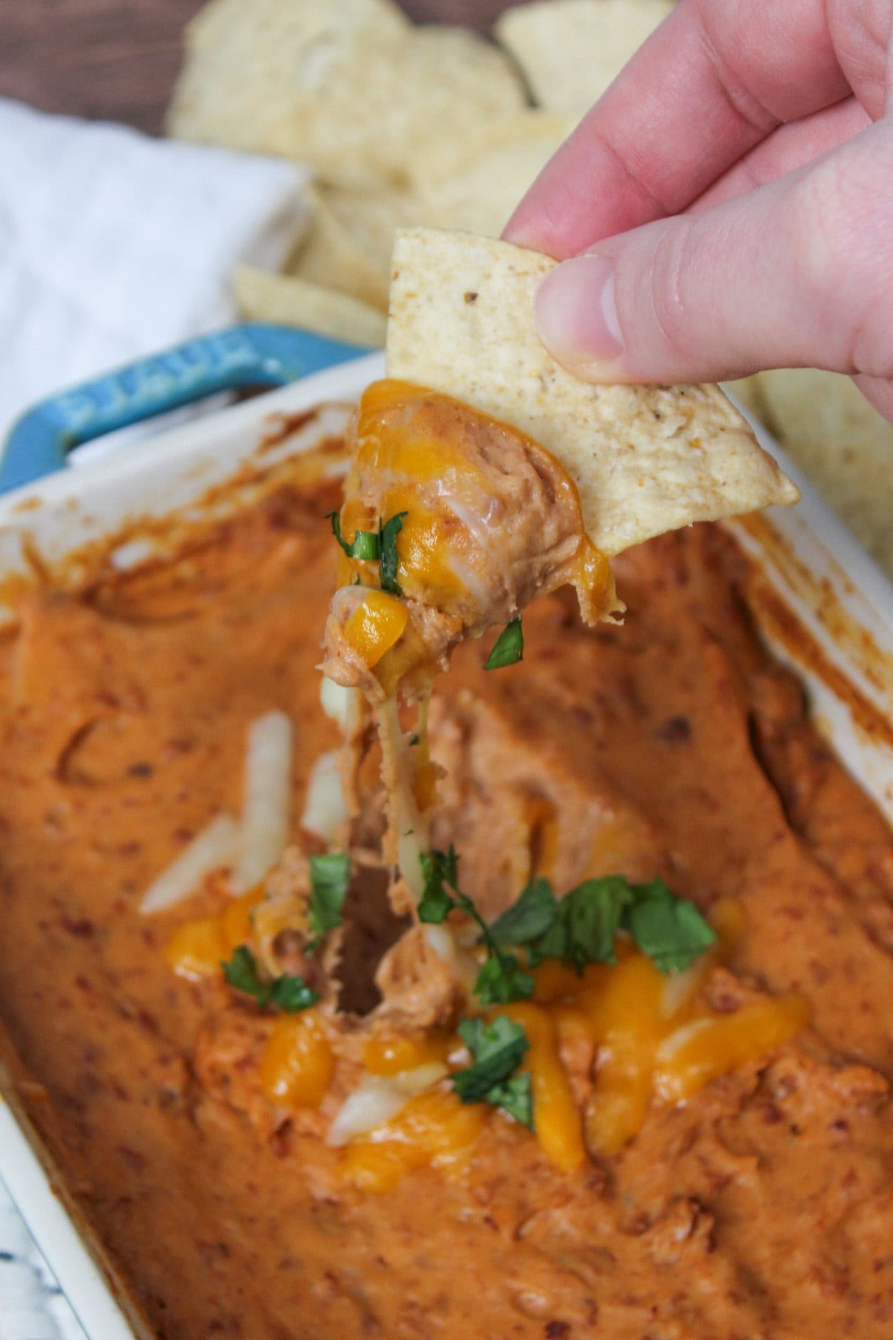 Cheesy Mexican bean dip being scooped up with a tortilla chip creating a wonderful cheese pull.