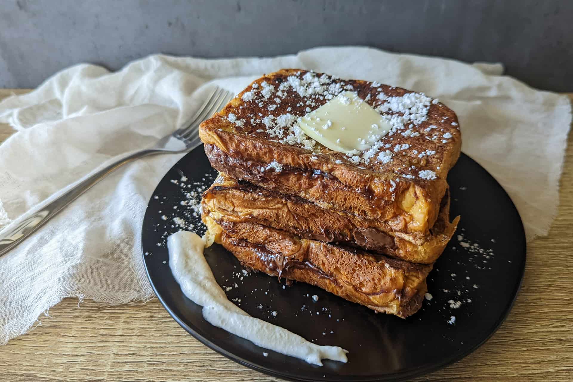 Two pieces of Nutella stuffed brioche french toast stacked on a plate