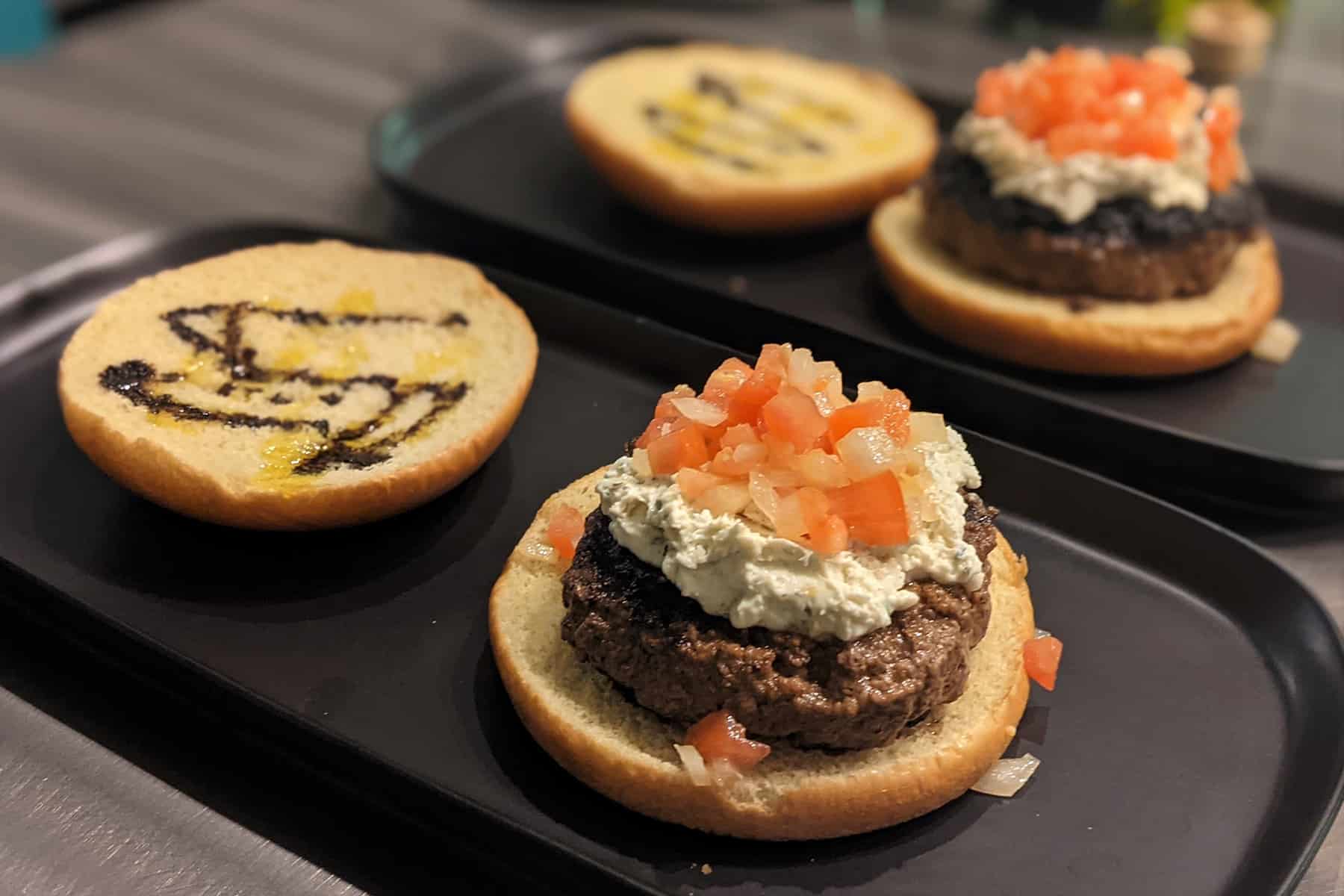 Burgers topped with cheese spread and bruschetta on a brioche bun drizzled with olive oil and balsamic