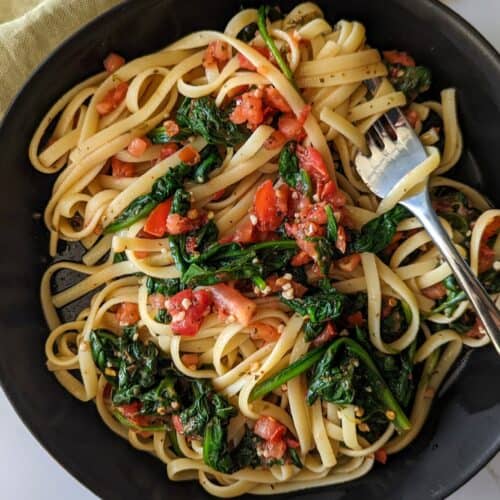 A bowl of spinach tomato pasta with olive oil in a bowl