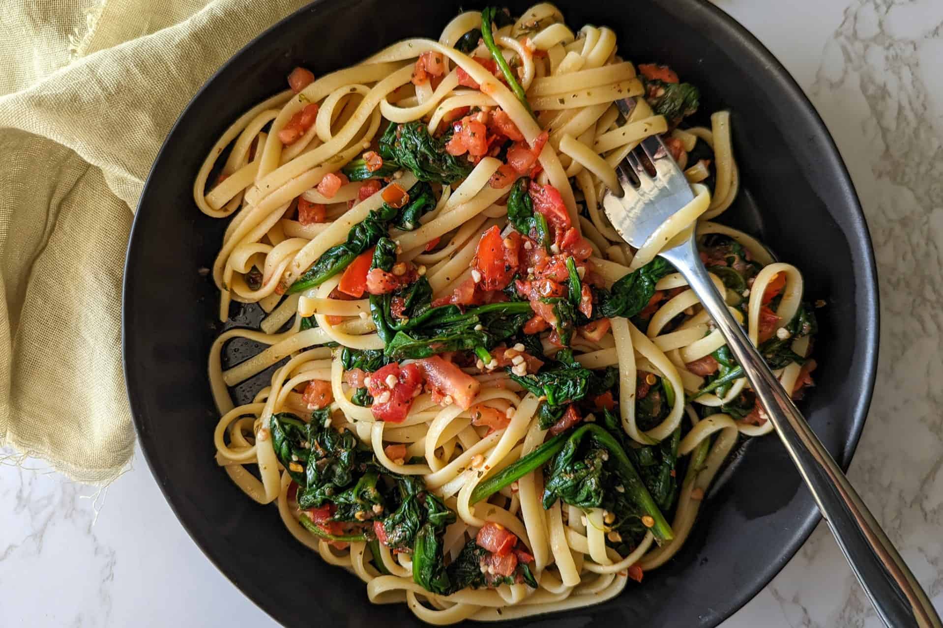 A bowl of spinach tomato pasta with olive oil in a bowl