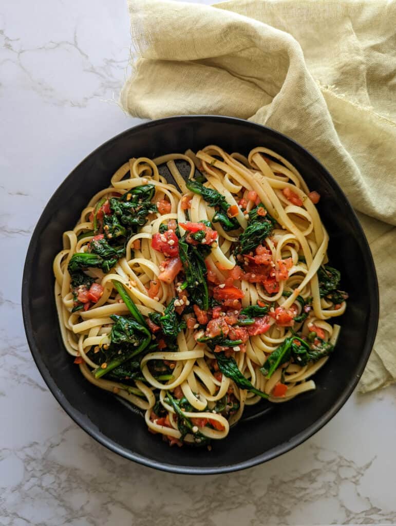 Spinach and tomato on top of linguine pasta in a bowl