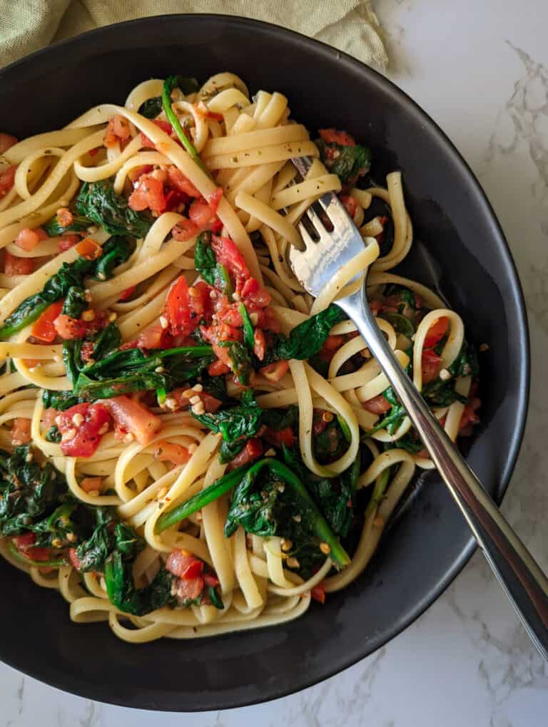 A bowl of linguine topped with spinach and tomatoes