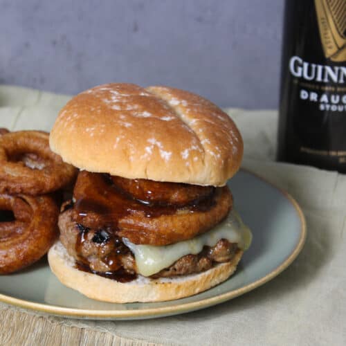 A burger topped with cheese, onion rings, and Guinness glaze on a potato bun