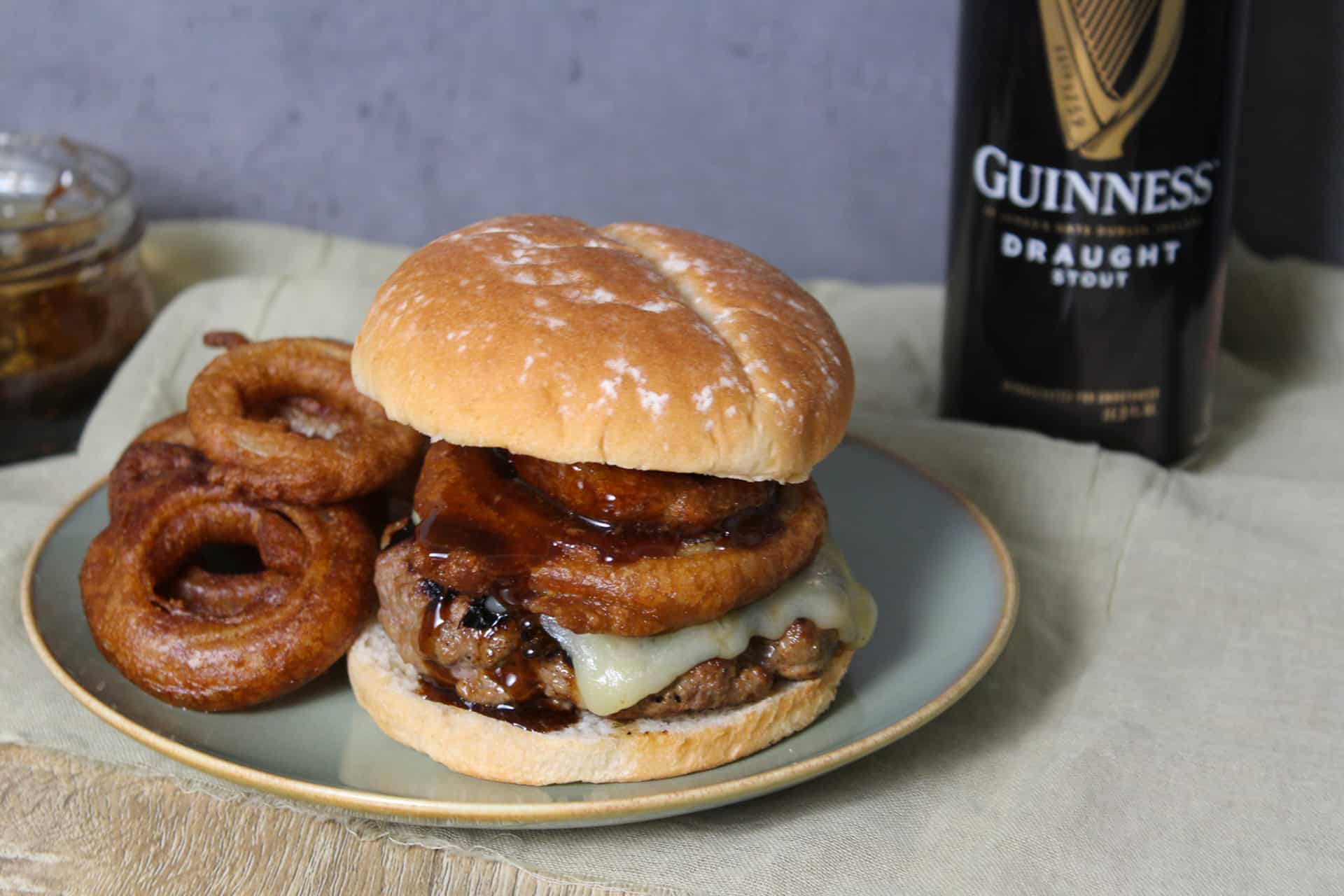 A burger topped with cheese, onion rings, and Guinness glaze on a potato bun
