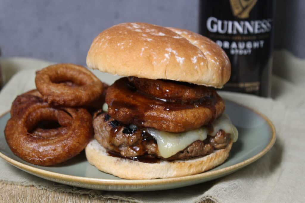 A Guinness burger topped with onion rings and cheddar cheese on a potato bun