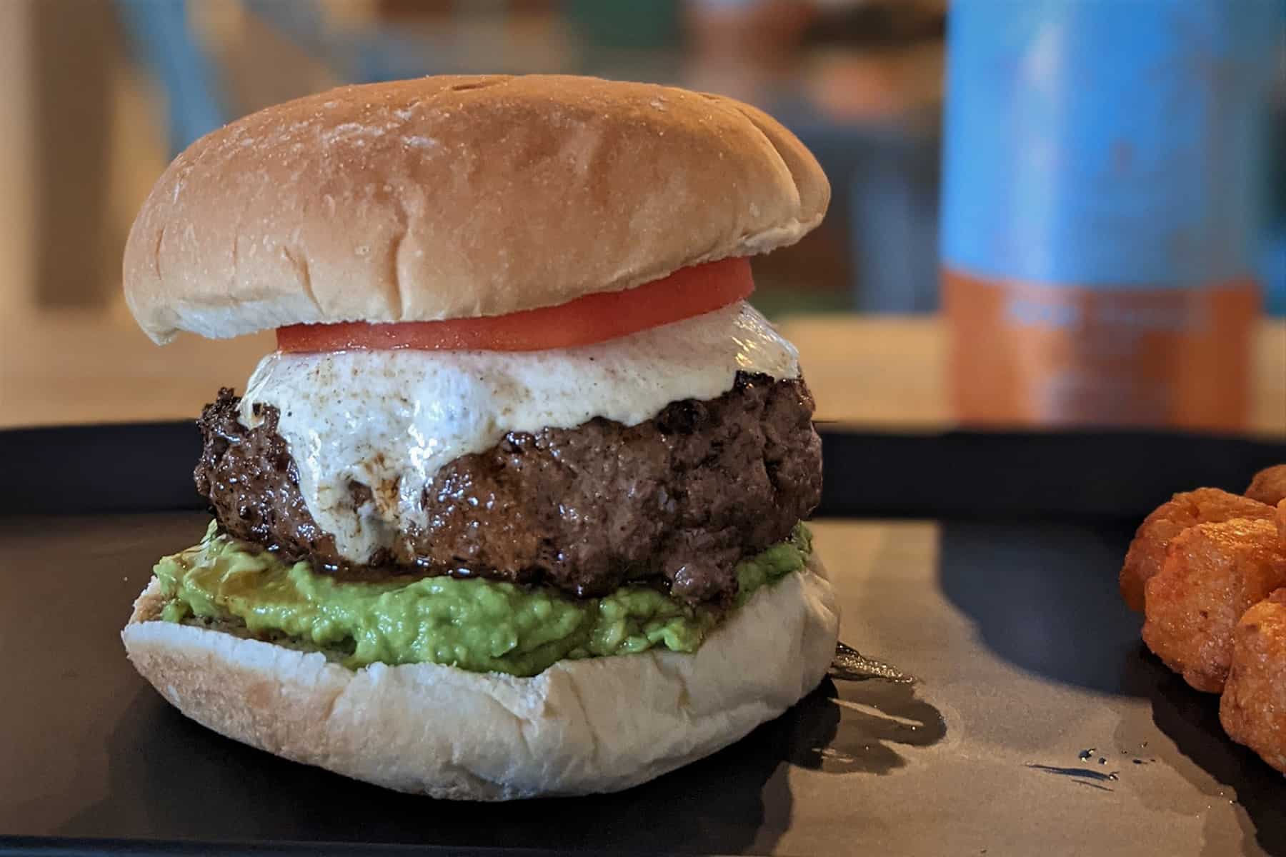 A juicy burger topped with mozzarella cheese, a fresh tomato slice, and mashed avocado