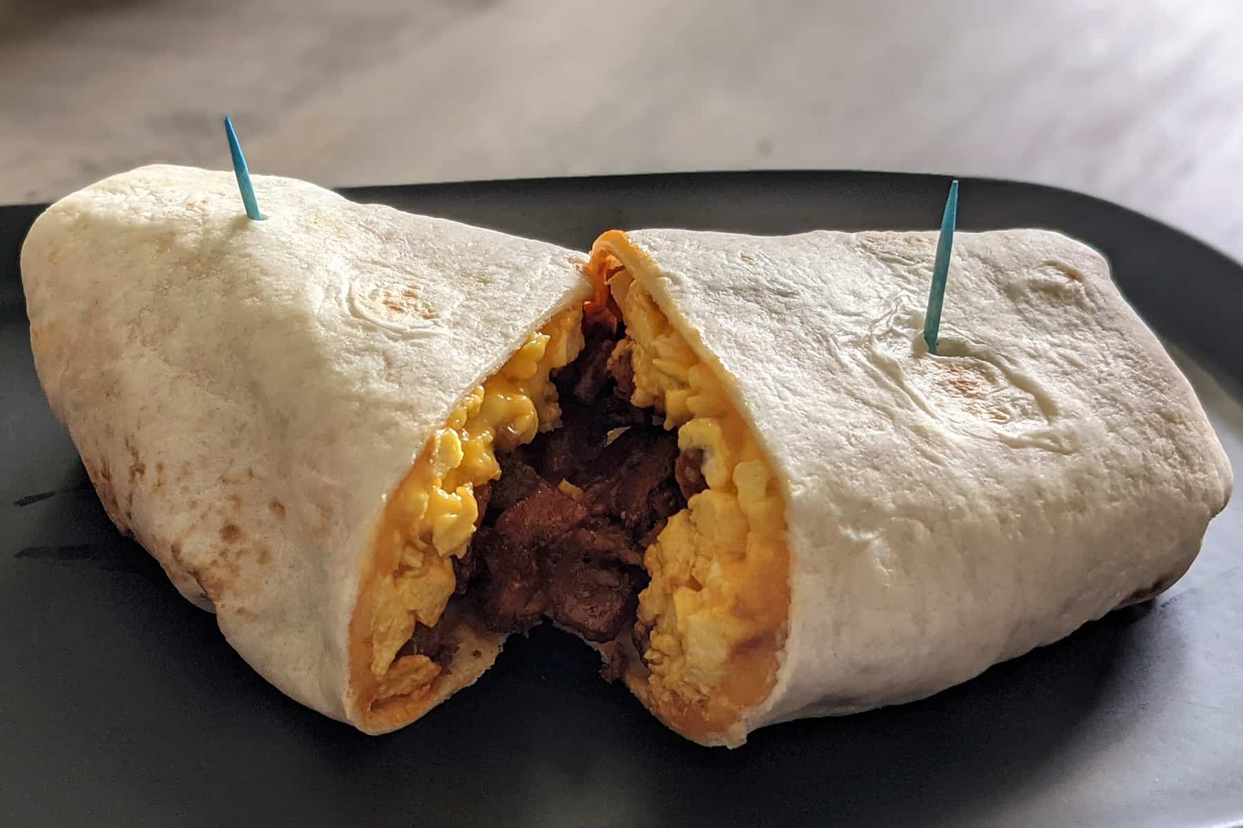 A breakfast wrap cut in half to show the inside filled with cheesy eggs, bacon, fried potatoes, and hot sauce