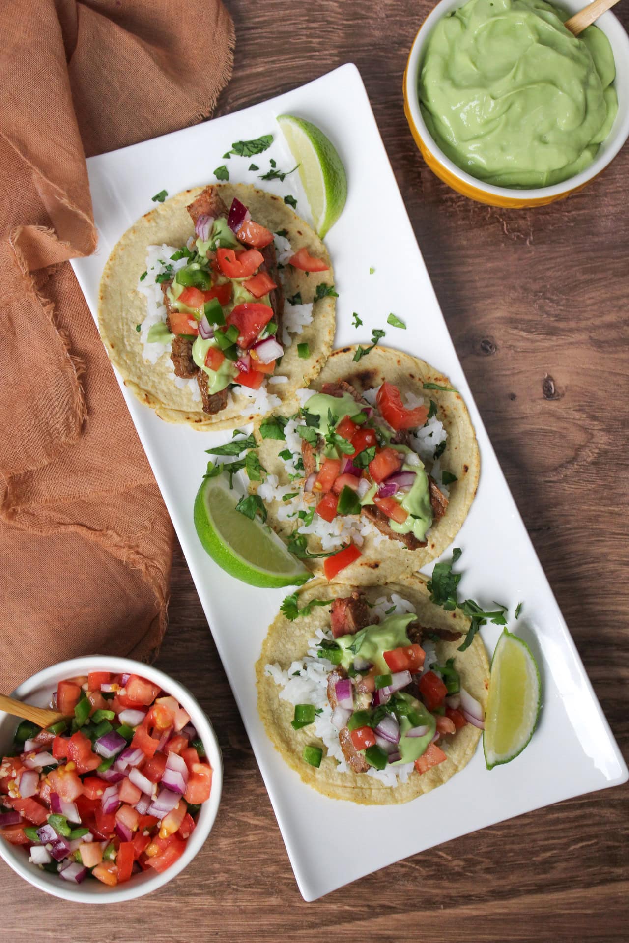 Carne asada street tacos on a plate topped with avocado crema and pico de gallo.