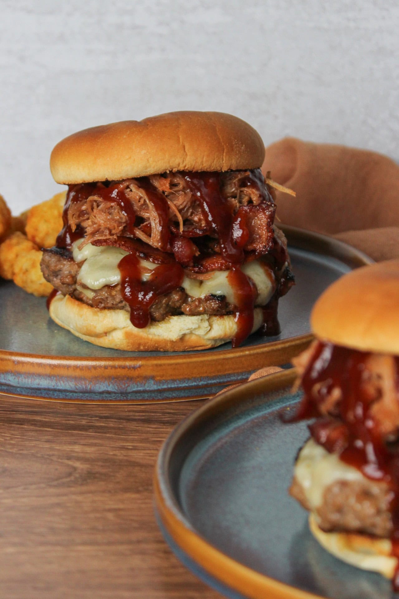 Two pulled pork burgers dripping with a sweet BBQ sauce and topped with bacon.