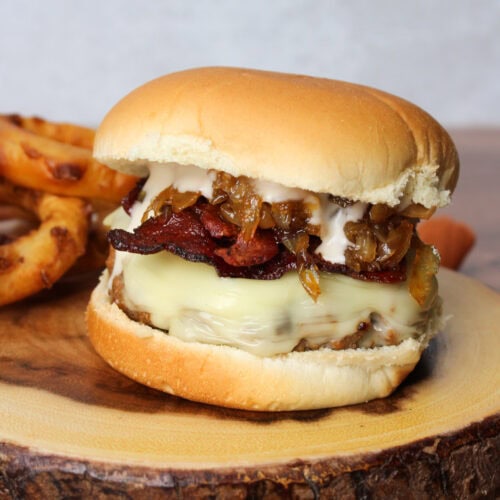 A burger with bacon, cheese, caramelized onions, and garlic aioli.