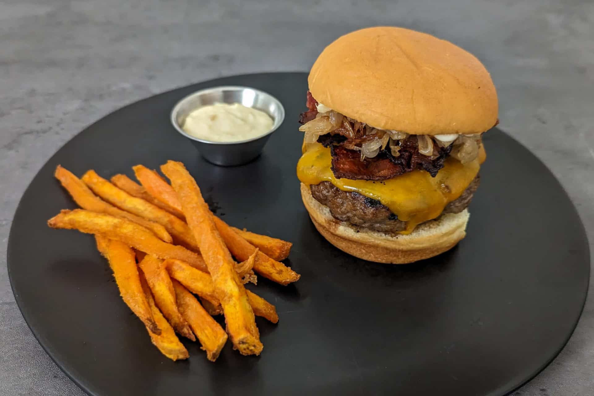 A bacon cheeseburger with roasted garlic aioli and caramelized onions served with sweet potato fries
