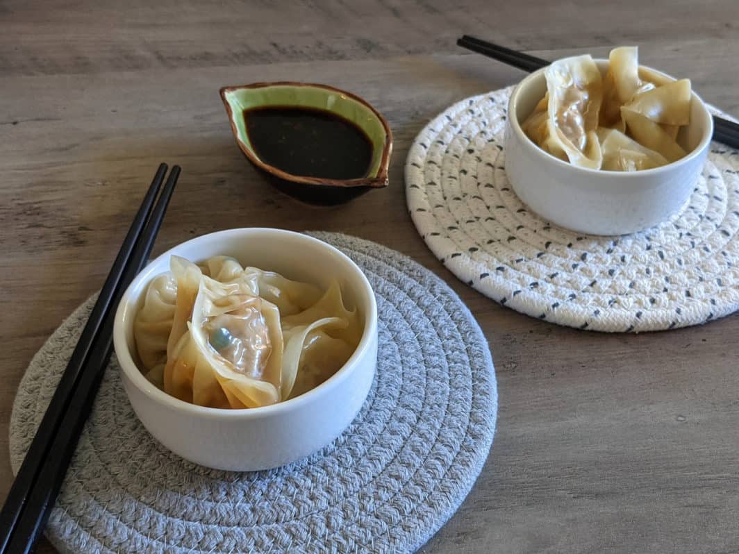Two serving dishes of steamed dumplings, with chopsticks and a dipping sauce
