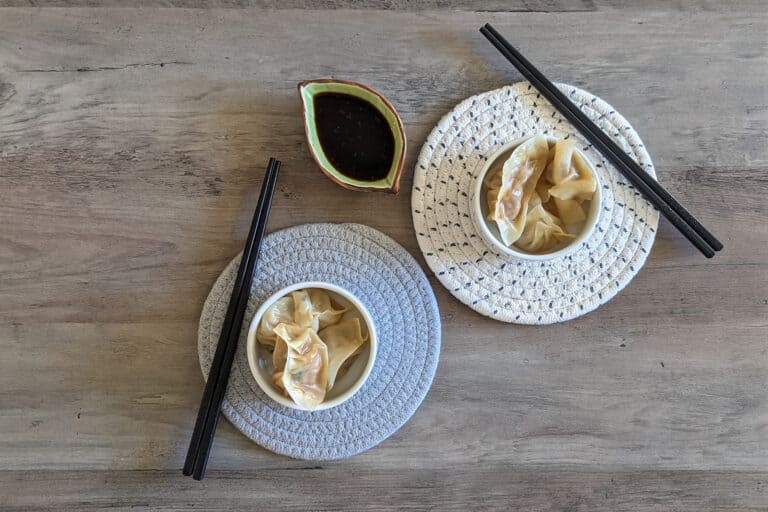Two serving dishes of steamed dumplings, with chopsticks and a dipping sauce