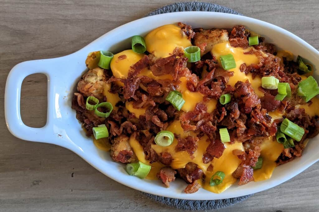 Loaded tater tots with melted Velveeta cheese, crispy crumbled bacon, and scallions in a serving dish