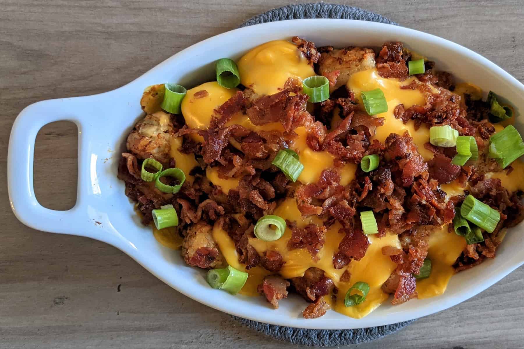 Loaded tater tots with melted Velveeta cheese, crispy crumbled bacon, and scallions in a serving dish