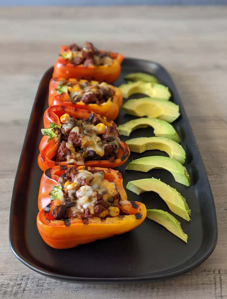 Bell peppers stuffed with chorizo, black beans, and veggies served with sliced avocado