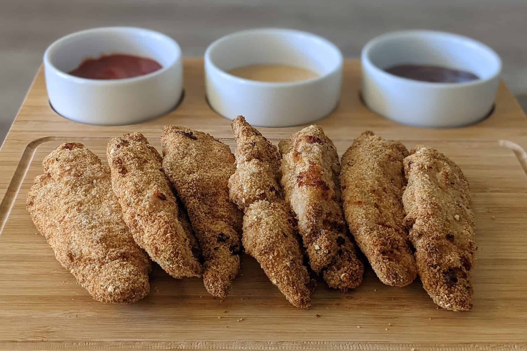 Air fryer chicken tenders on a serving platter, served with ketchup, honey mustard, and bbq sauce