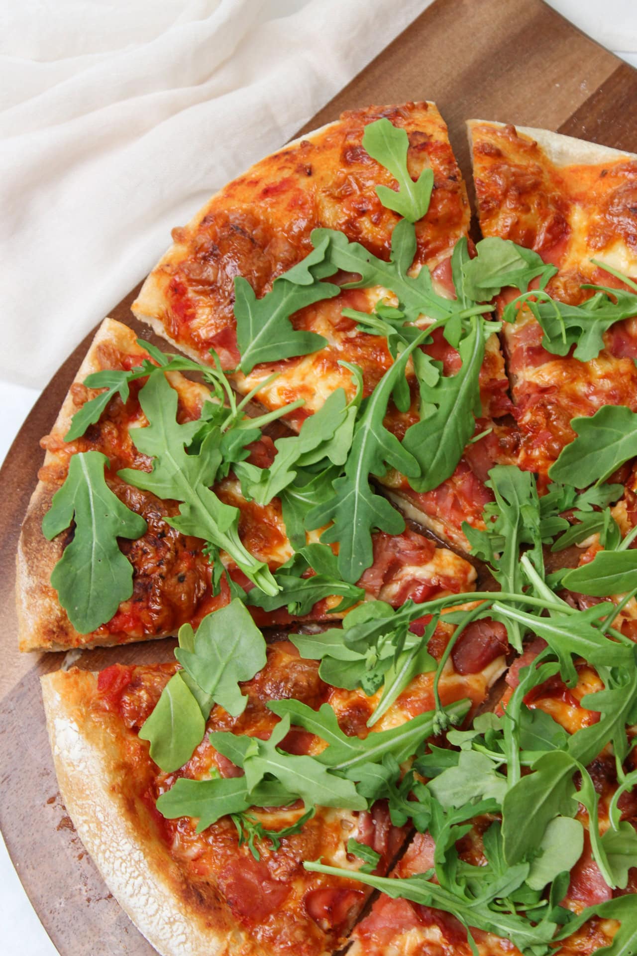 A pizza on a wooden cutting board topped with crispy prosciutto and fresh arugula. 