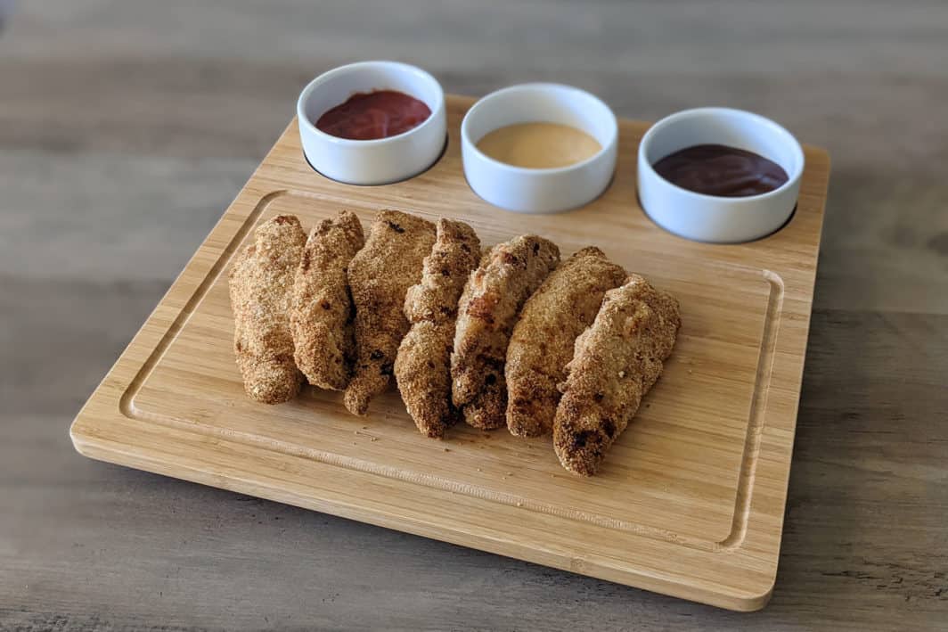 Air fryer chicken tenders on a serving platter, served with ketchup, honey mustard, and bbq sauce