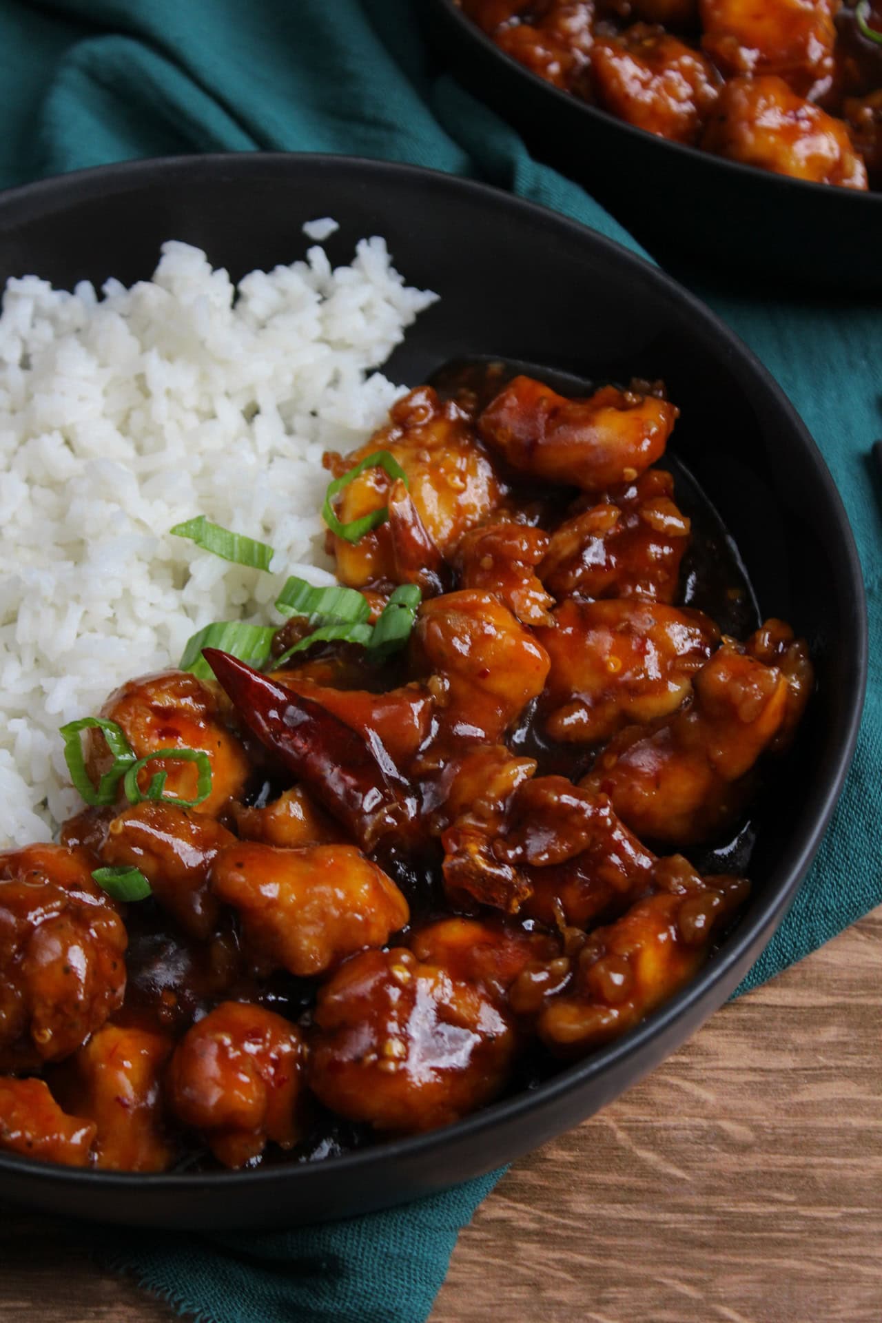 Super saucy spicy general tso's chicken with steamed white rice in a black bowl.