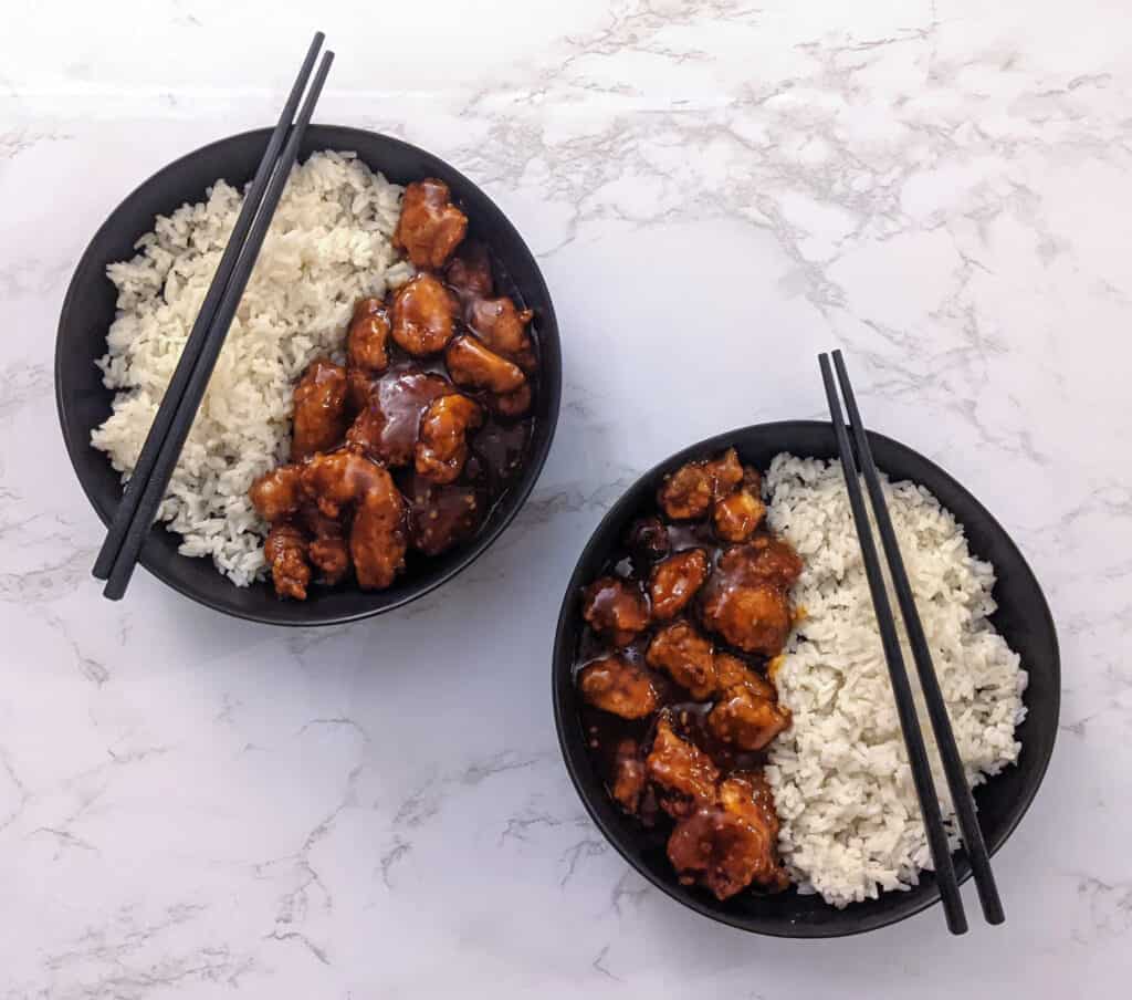 Two bowls of crispy general tso chicken with white rice and chopsticks