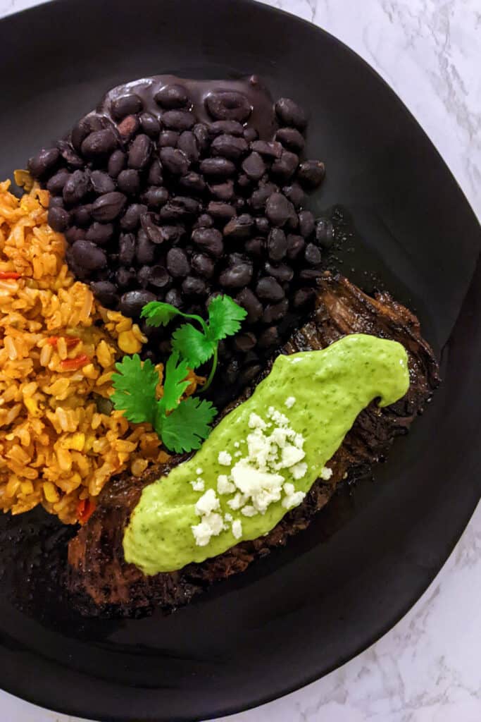 Carne asada steak topped with cilantro-lime crema and queso fresco, served with rice and beans