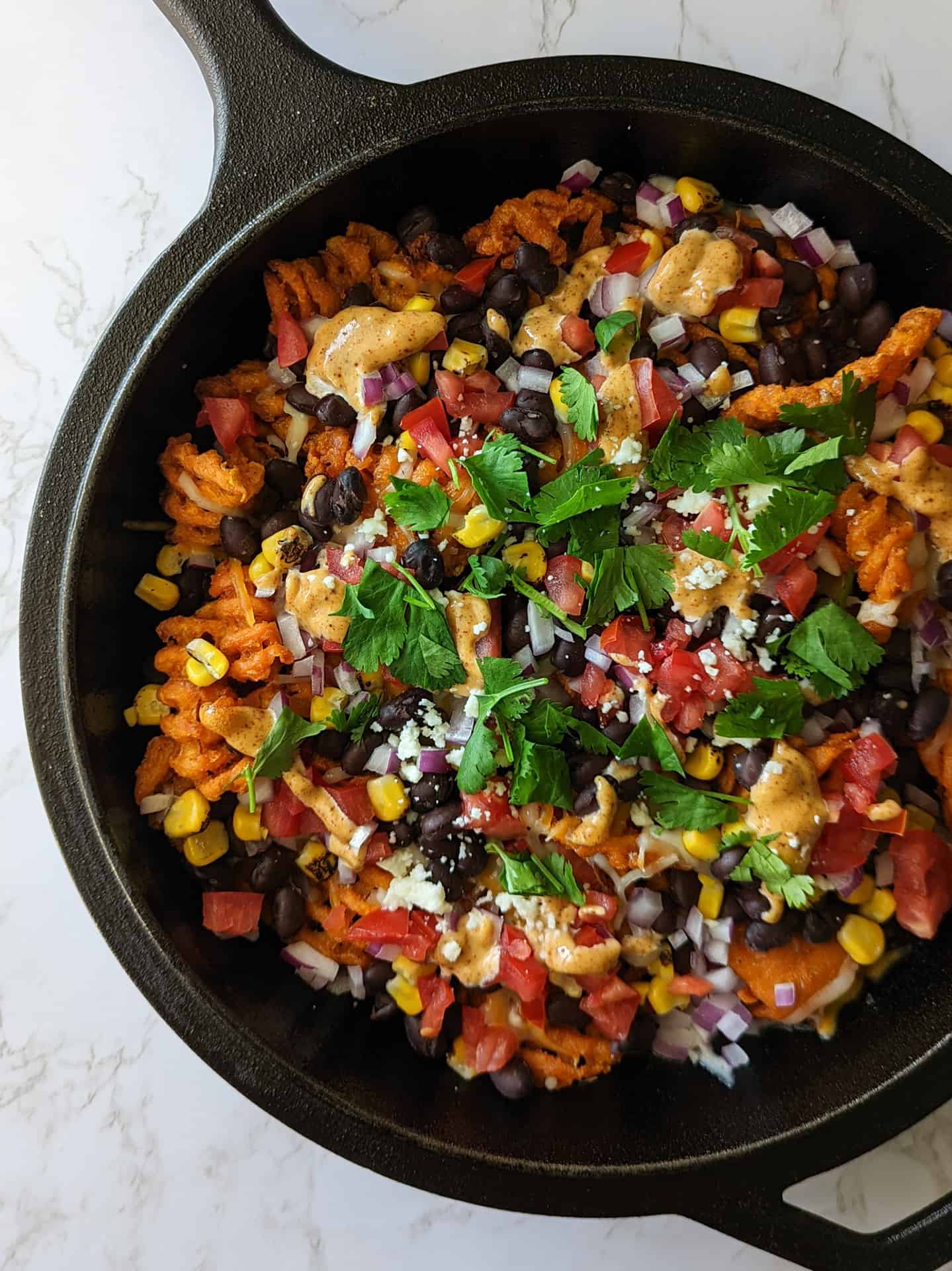 A cast iron skillet with loaded sweet potato waffle fries