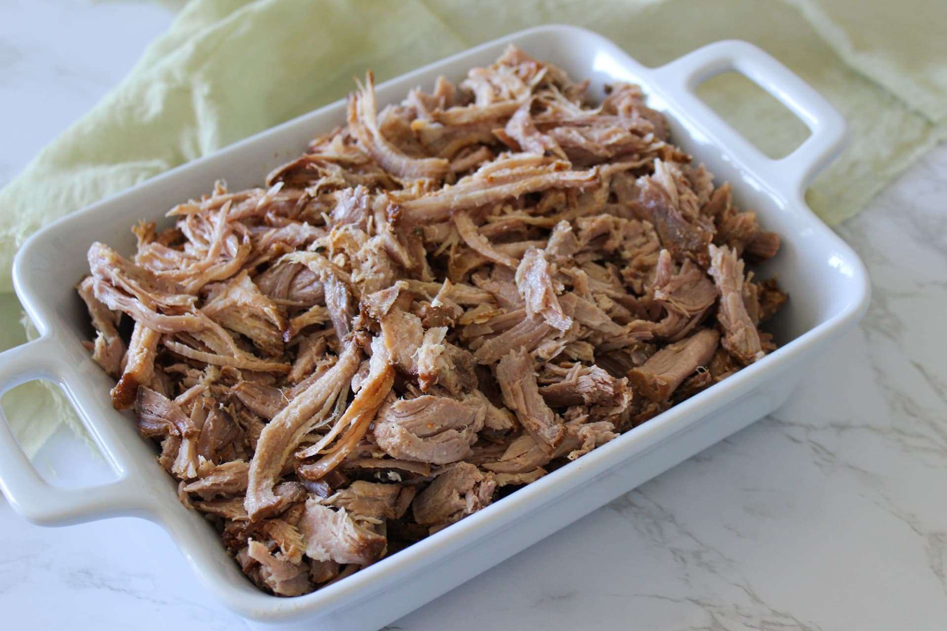 A serving dish of slow cooker carnitas, pulled by hand