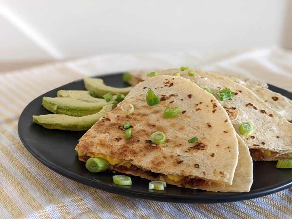 A breakfast quesadilla of bacon, eggs, and cheese served with fresh avocado