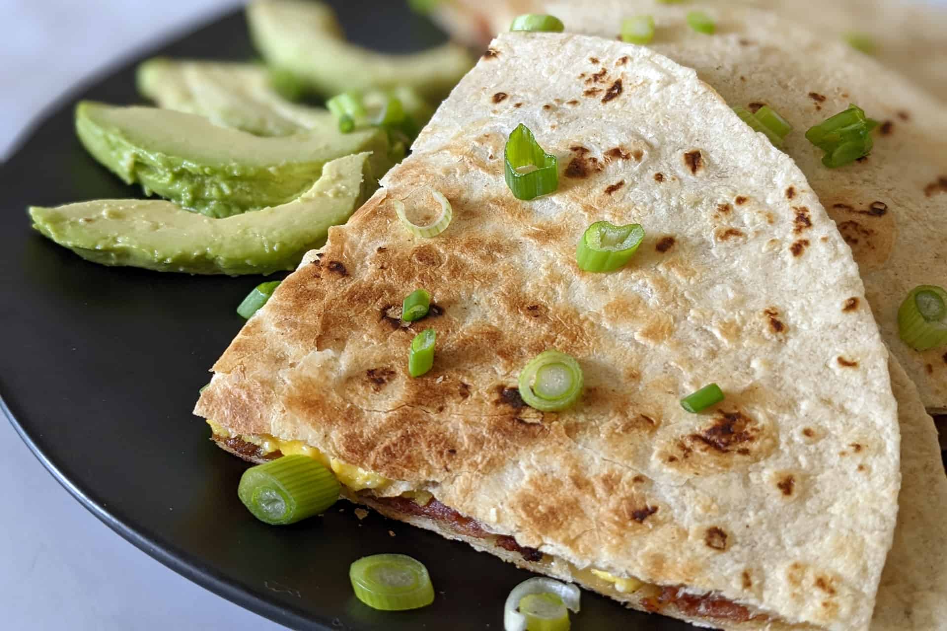 A breakfast quesadilla with bacon, eggs, and cheese, served with fresh avocado