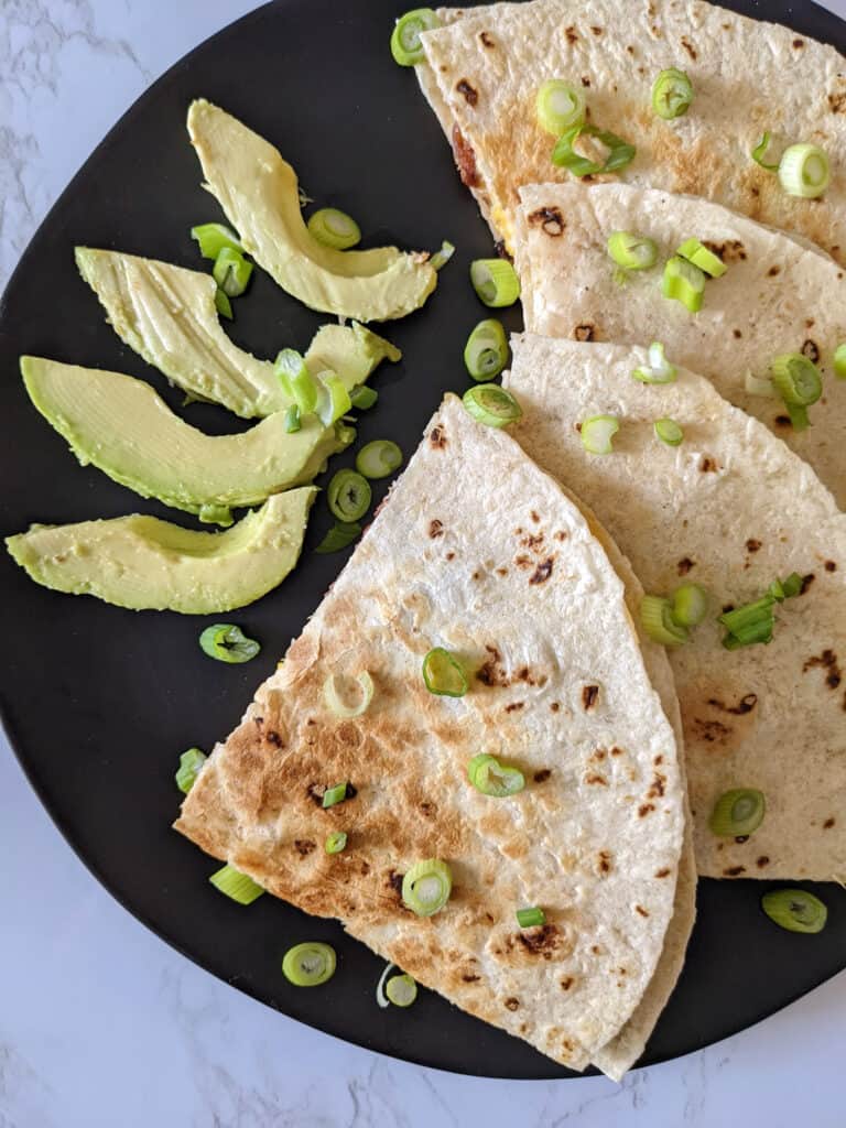 A breakfast quesadilla sliced and served on a plate with fresh avocado