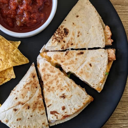 A chicken and cheese quesadilla on a plate with chips and salsa
