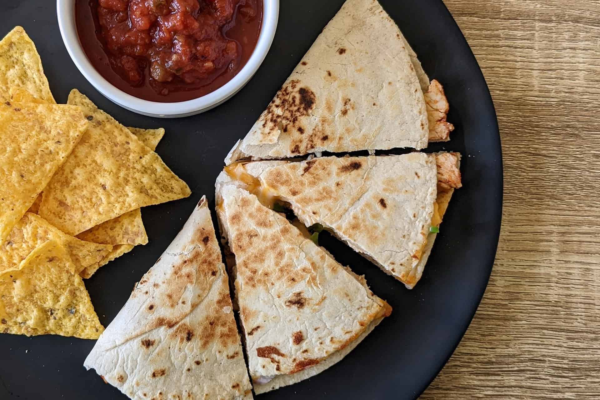 A chicken and cheese quesadilla on a plate with chips and salsa