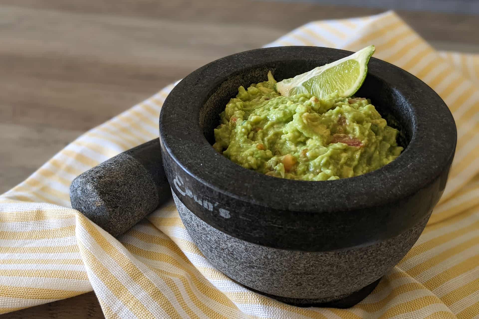 Fresh guacamole in a mortar and pestle garnished with a lime