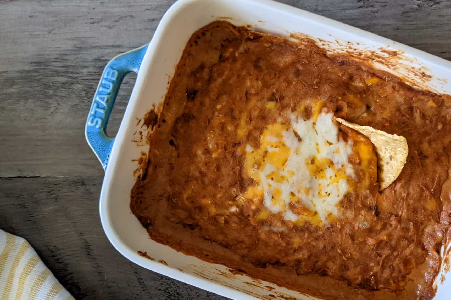Oven-baked bean dip garnished with cheese and a tortilla chip