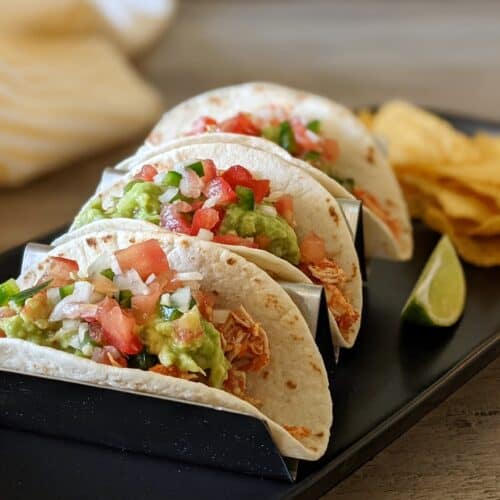 A plate of shredded chicken tacos with pico de gallo and guacamole