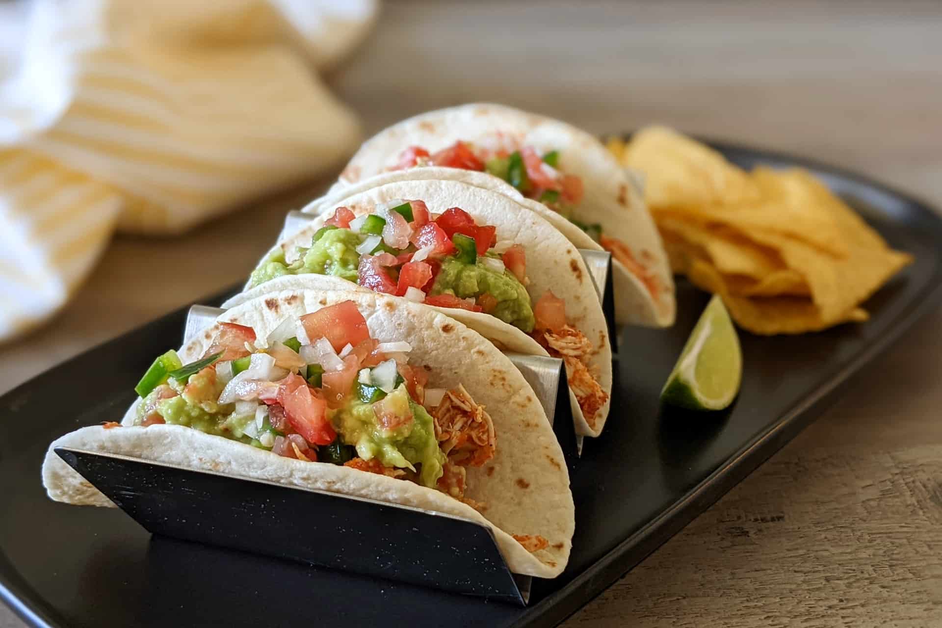 A plate of shredded chicken tacos with pico de gallo and guacamole