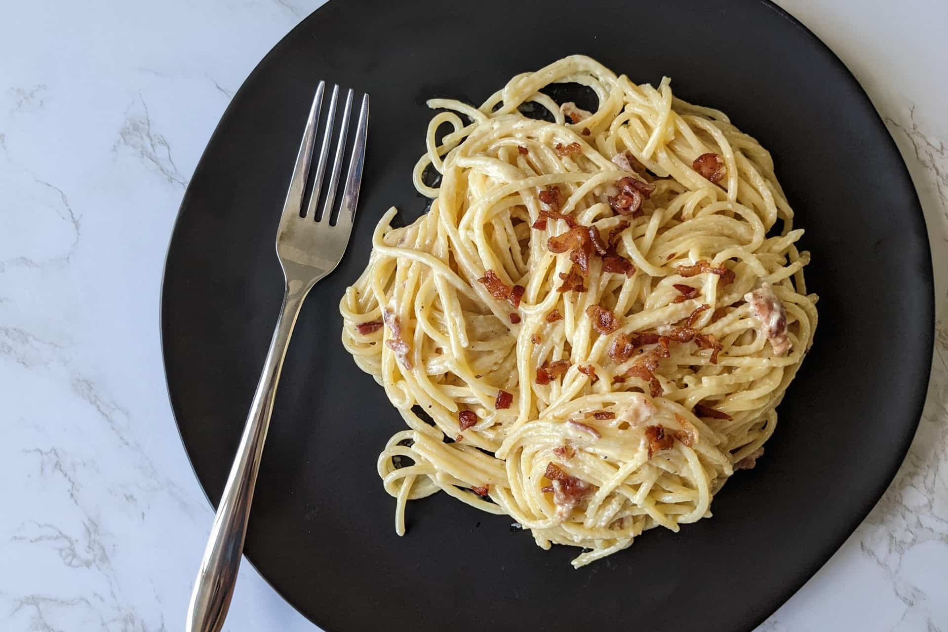 A plate of spaghetti carbonara made with crumbled bacon