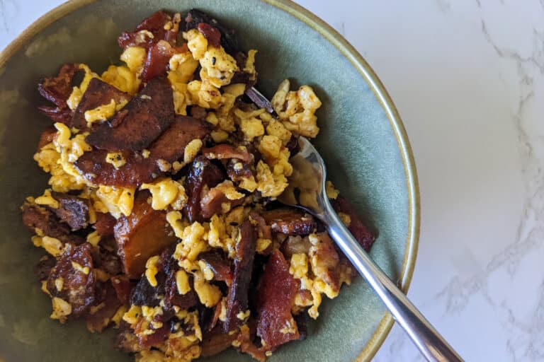 A bowl of bacon, eggs, potatoes, and cheese with hot sauce