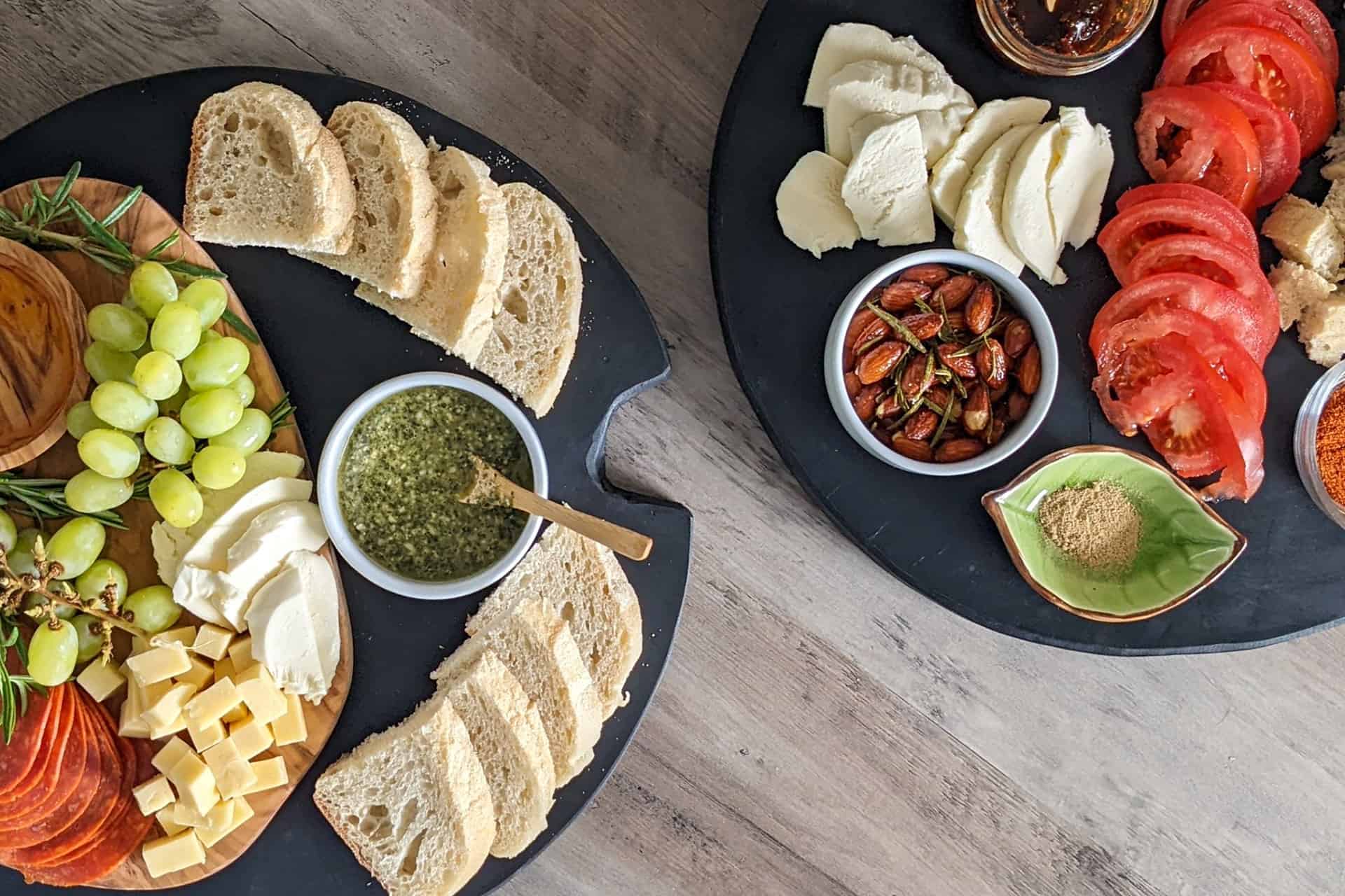 Two charcuterie boards with bread, cheese, fruit, nuts, and spreads