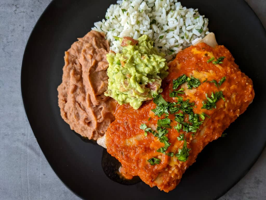 A plate of chicken burritos ranchero with rice, beans, and guac