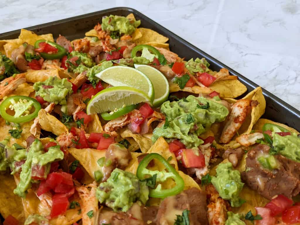 A sheet pan of loaded nachos with lime wedges