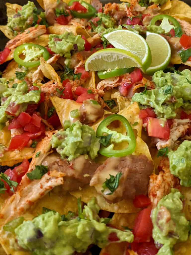 A sheet pan of loaded nachos with beans, guac, cheese, chicken, and tomato