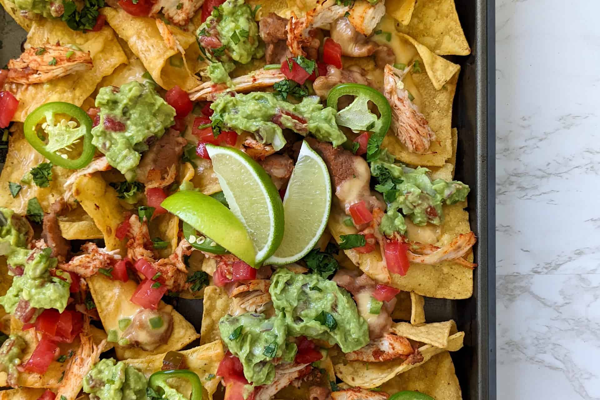 Loaded sheet pan nachos with chicken, guac, beans, cheese, and tomatoes