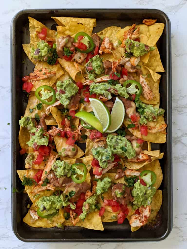 Loaded sheet pan nachos garnished with lime wedges