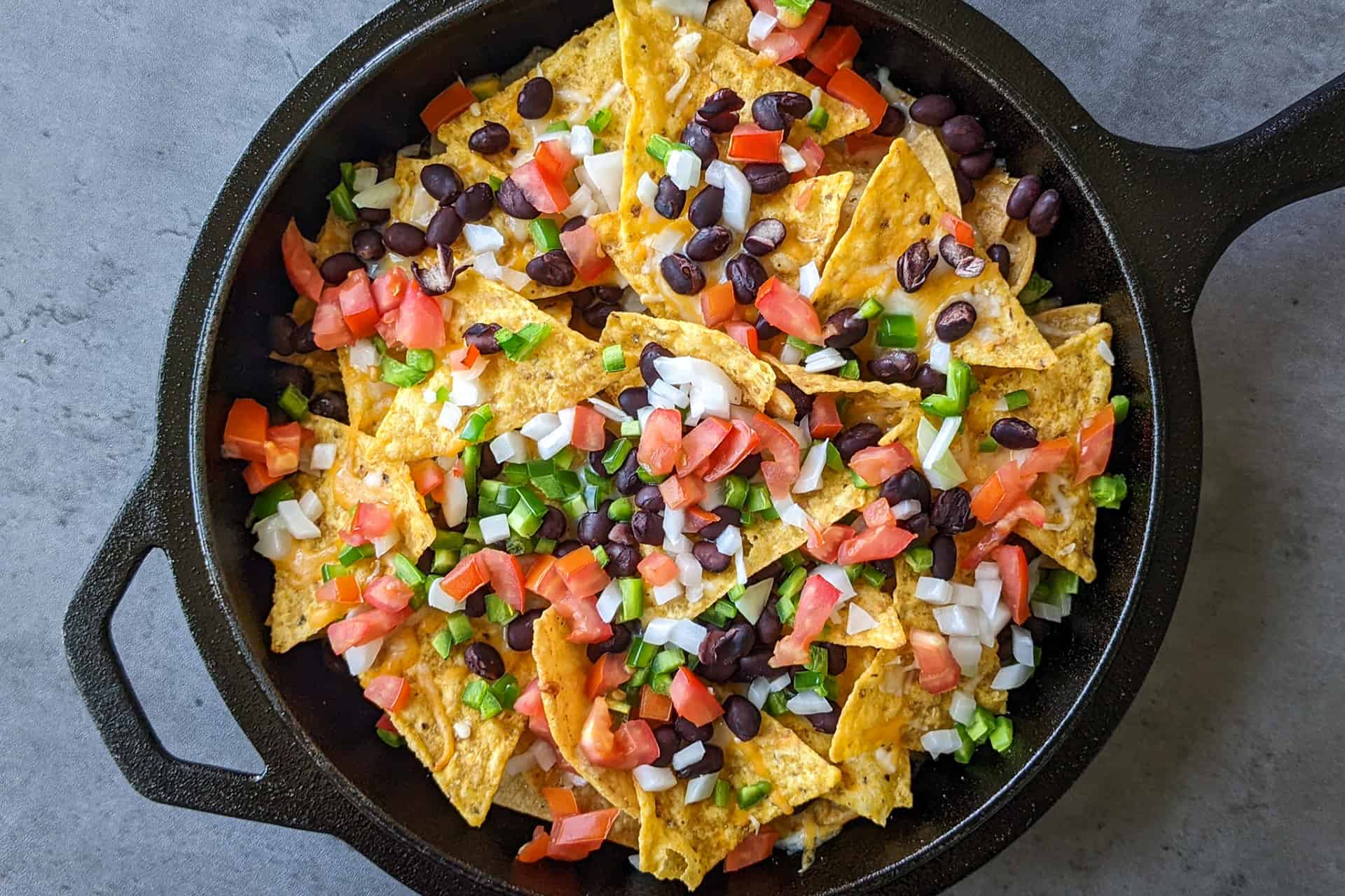 Nachos topped with cheese and fresh produce in a cast iron skillet