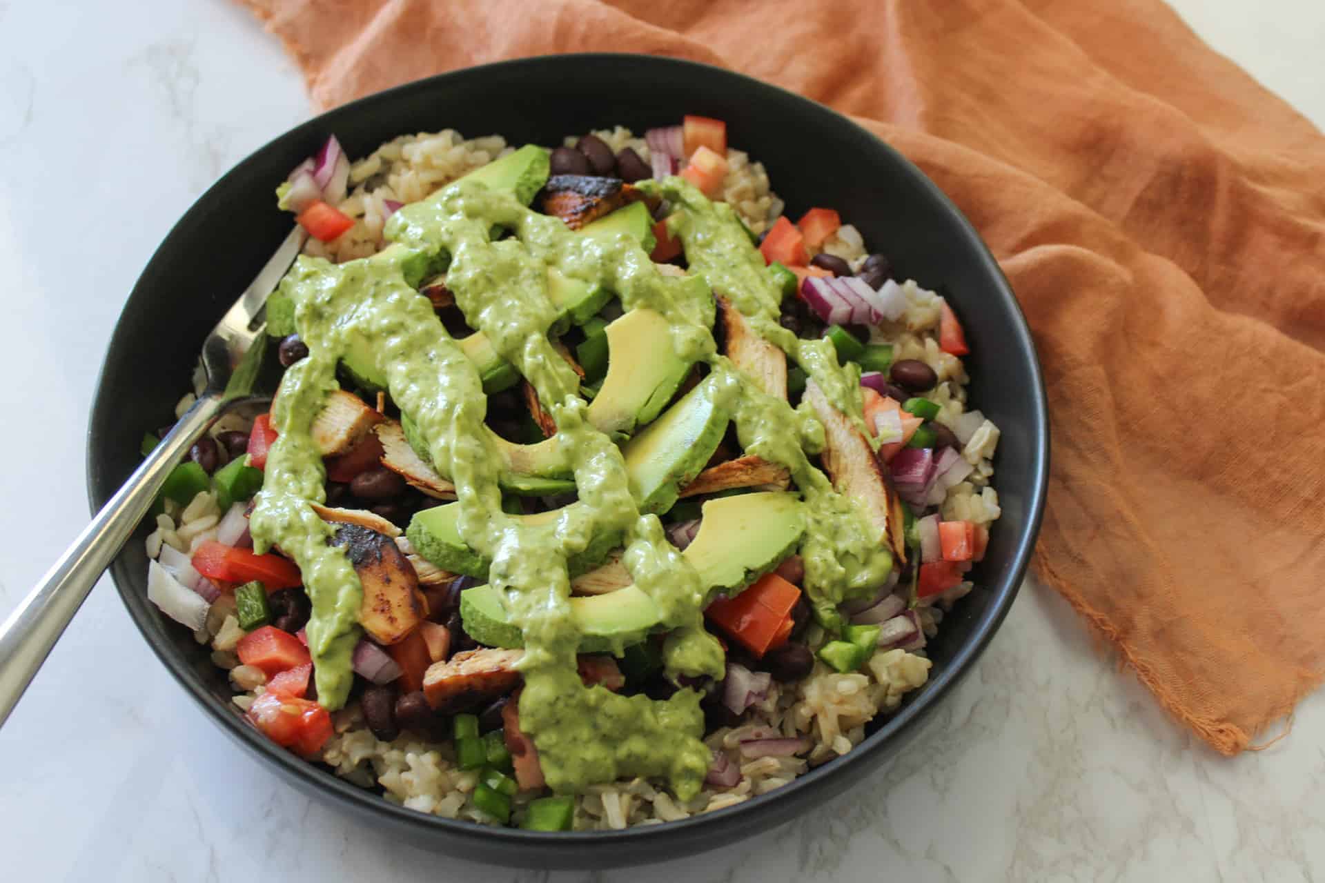 A chili lime chicken burrito bowl topped with avocado and cilantro lime crema