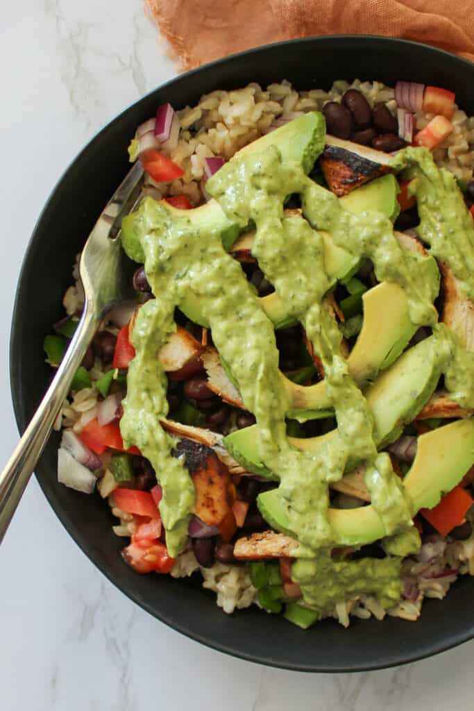 A healthy chili lime grilled chicken burrito bowl topped with avocado crema
