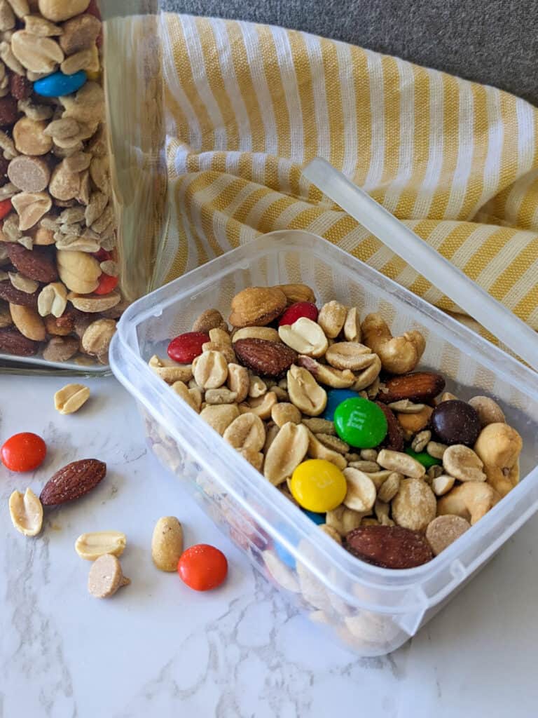 A container of sweet and salty trail mix with M&M's, peanut butter chips and mixed nuts